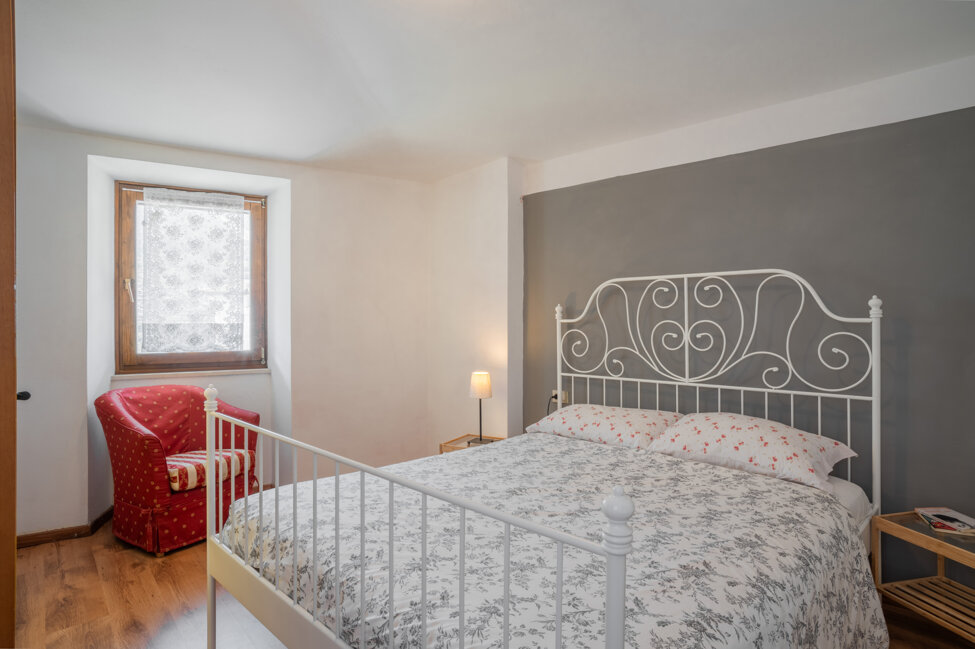 Camera da letto con letti in ferro battuto e poltrona rossa in appartamento sul Lago di Garda