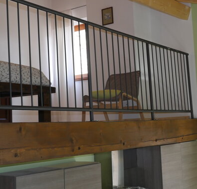 Zona soppalco di un appartamento vacanze con letto e sedia Zona soppalco di un appartamento vacanze con letto e sedia