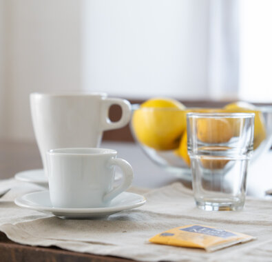 Colazione con tazze di caffè e bicchiere su tavolo, limoni in sfondo Colazione con tazze di caffè e bicchiere su tavolo, limoni in sfondo