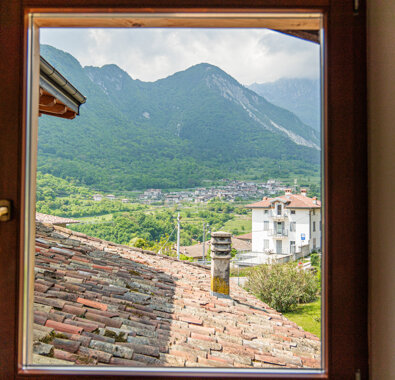 Vista da una finestra su una vallata montana con case e natura, cielo nuvoloso
