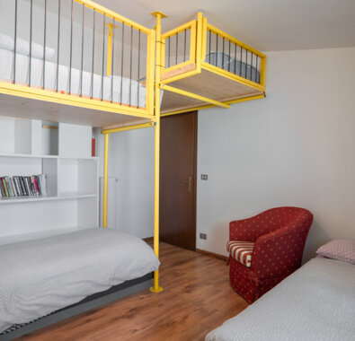 Camera da letto moderna con letto a soppalco giallo, poltrona rossa e scaffali con libri Camera da letto moderna con letto a soppalco giallo, poltrona rossa e scaffali con libri