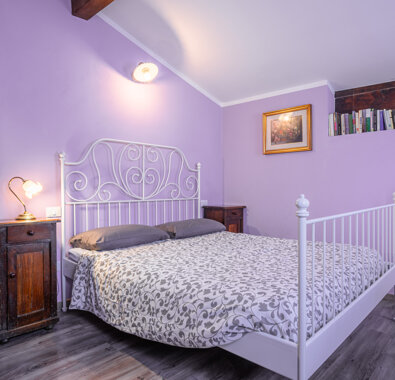 Camera da letto con pareti lilla, letto matrimoniale e armadio in legno