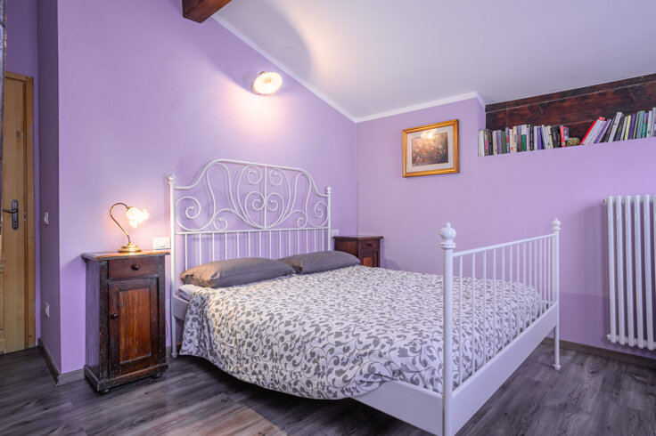 Camera da letto in appartamento lilla con letto matrimoniale e comodini, decorazioni e libri su mensola