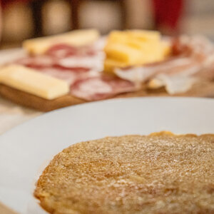 Piatto con frittella di patate e tagliere di salumi e formaggi sullo sfondo Piatto con frittella di patate e tagliere di salumi e formaggi sullo sfondo