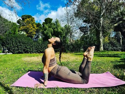 Donna che pratica yoga su un tappetino rosa in un parco verde.