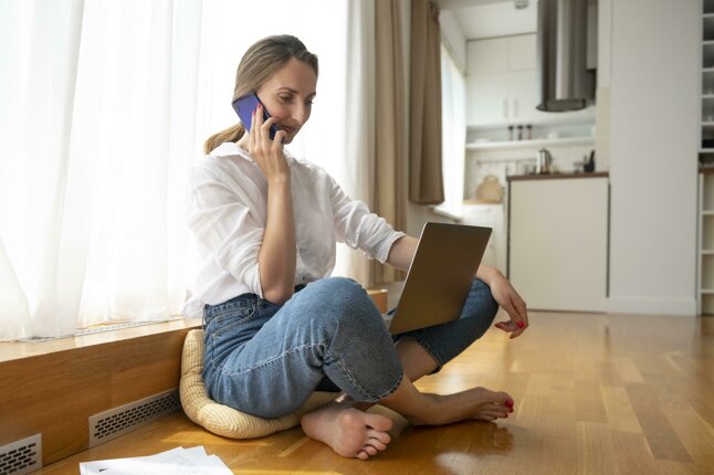 Donna al telefono mentre lavora al laptop in una cucina luminosa