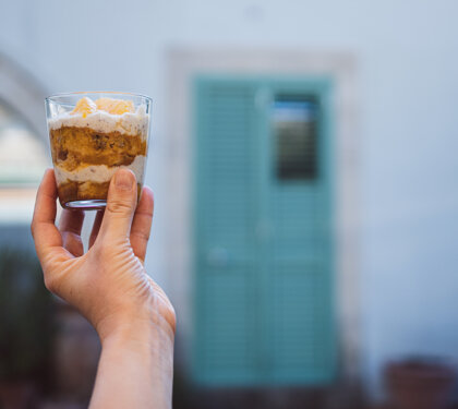 Dessert in bicchiere tenuto in mano davanti a una porta azzurra sfocata Dessert in bicchiere tenuto in mano davanti a una porta azzurra sfocata