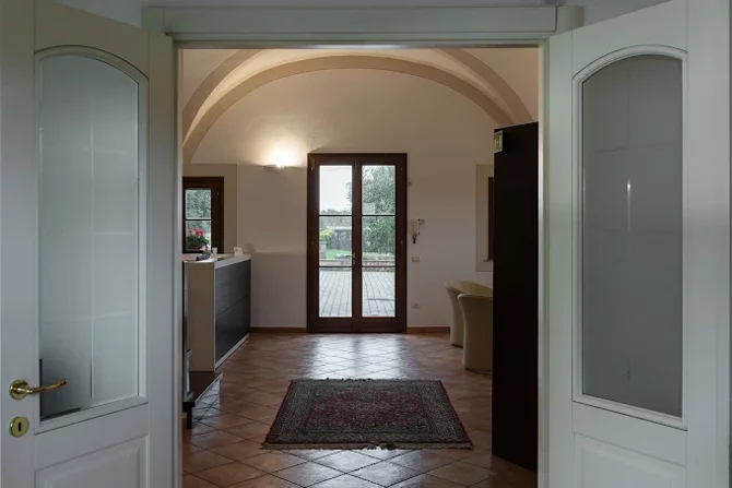 Vista di un ingresso elegante con pavimento in piastrelle e tappeto, porte aperte e luce naturale proveniente da una finestra.