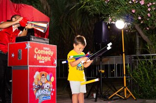 bambino sul palco con numerose bacchette magiche colorate
