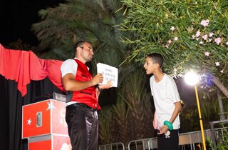 Mago Taz fa leggere un cartello a un giovane assistente durante un gioco di illusionismo