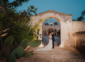 Bride and groom embracing under a stone archway in a Sicilian wedding setting.