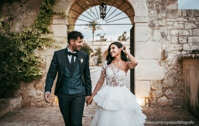 Smiling couple in elegant wedding attire walking through a historic Sicilian venue