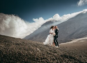 Couple embracing during a wedding photoshoot on a mountainside with dramatic clouds.