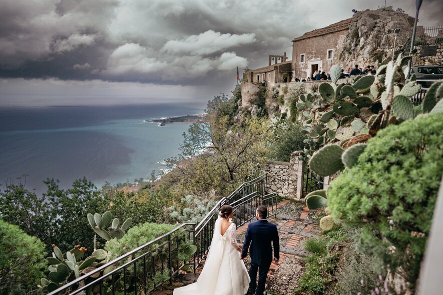 Luxury wedding couple descending steps with Sicilian coastal view