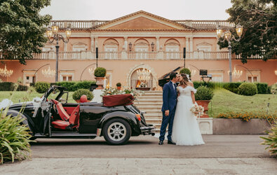 Luxury Sicilian wedding with couple kissing in front of elegant villa and vintage car