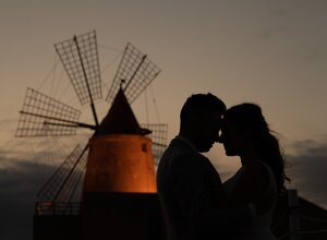 Silhouette of a couple embracing in front of a lit windmill at sunset, Sicily weddings.