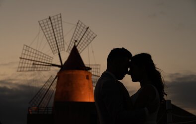 Silhouette of a couple at sunset with a traditional Sicilian windmill in the background, symbolizing luxury weddings and destination weddings in Sicily.