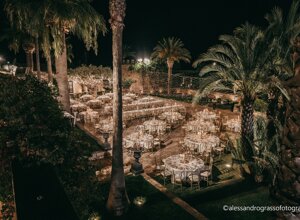 Elegant outdoor wedding reception setup in Sicily with round tables under palm trees and string lights