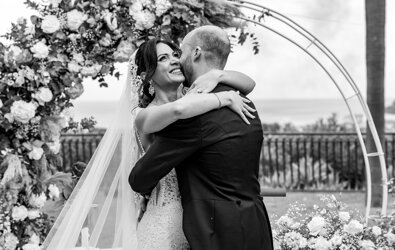 A joyful bride and groom embrace under a floral arch during a luxury Sicilian destination wedding.