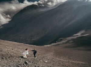 Couple in wedding attire on a rocky slope with a mountain in the background, Sicily destination wedding.