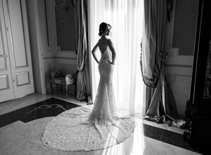 Bride in elegant wedding gown standing by window, Sicily destination wedding