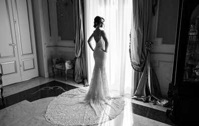 Bride in elegant lace wedding dress by a window, luxury Sicilian wedding setting.