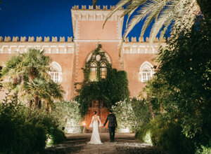 Couple walking towards a castle-like wedding venue in Sicily at night