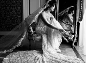 Bride getting ready in elegant lace dress with long veil beside mirror