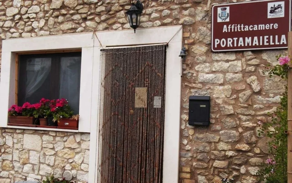 Ingresso affittacamere PortaMaiella con parete in pietra, fiori, e insegna.