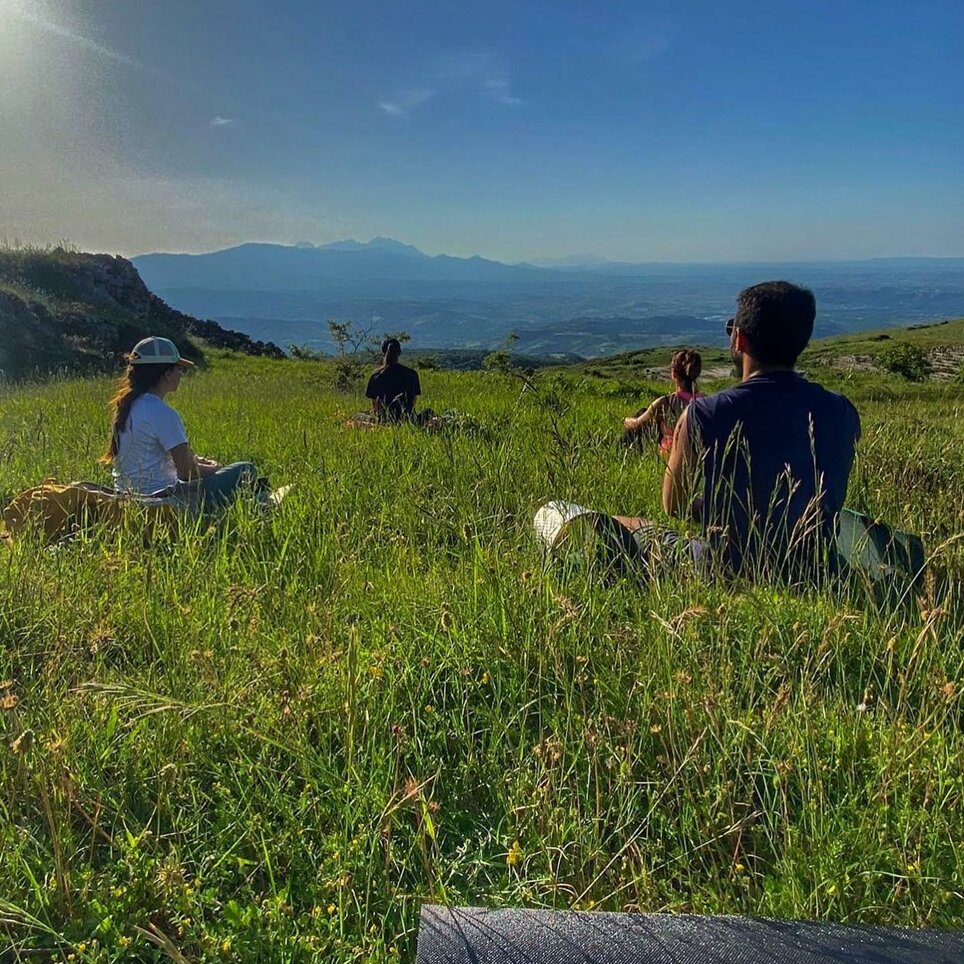 Persone sedute in un prato nel Parco Nazionale della Maiella, circondate dalla natura e dalle montagne sullo sfondo.