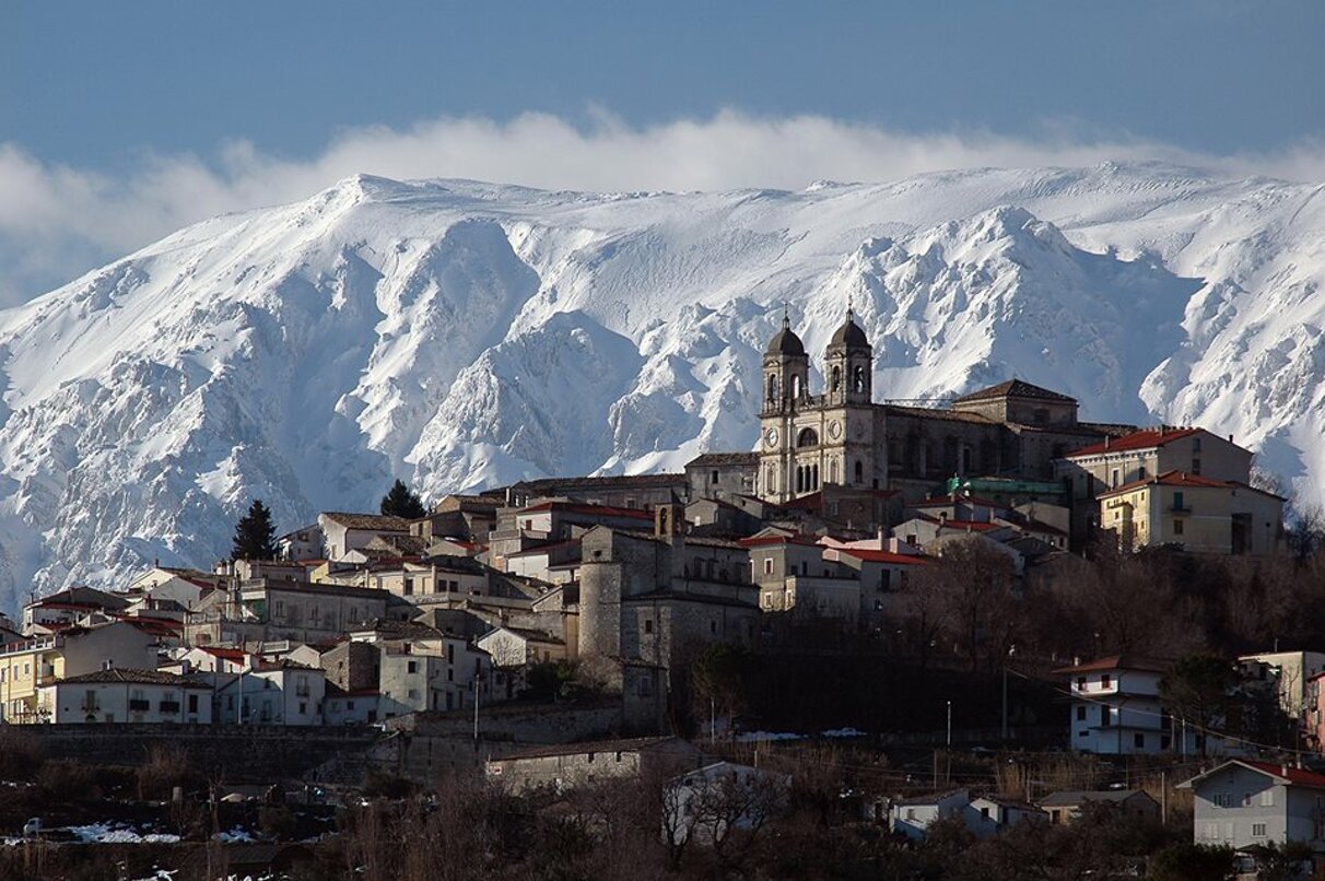 Veduta di un borgo montano abruzzese con colline innevate sullo sfondo