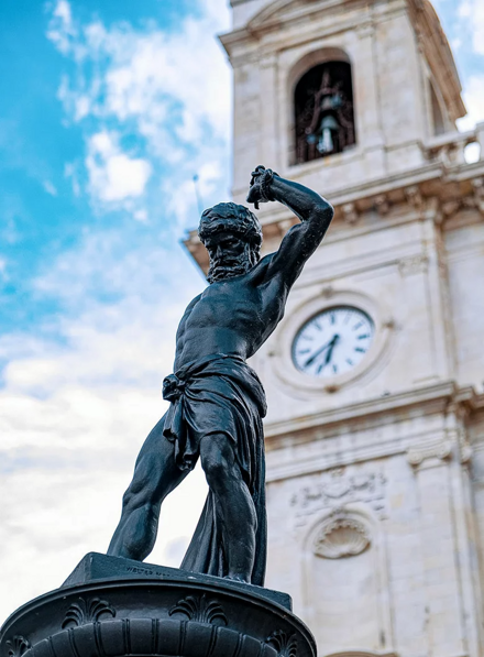 Statua di bronzo davanti a una torre con orologio nella piazza principale