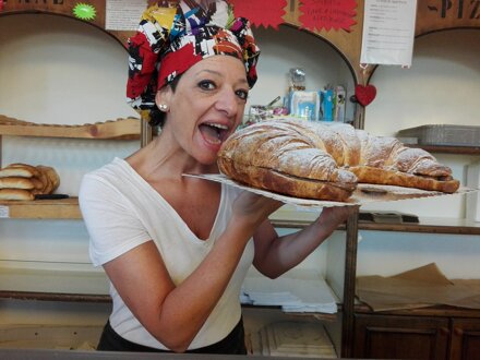 Panettiera sorridente mostra un enorme cornetto in una panetteria