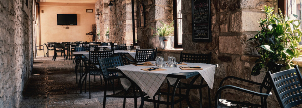 Sala interna di un ristorante con tavoli apparecchiati e pareti in pietra Sala interna di un ristorante con tavoli apparecchiati e pareti in pietra