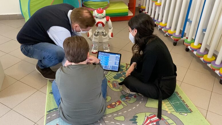 Adulti e bambino interagiscono con un robot umanoide in un ambiente educativo.