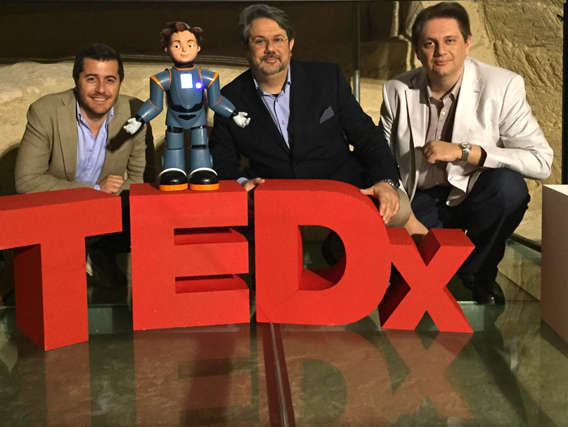 Tre uomini accanto a un robot su un palco TEDx