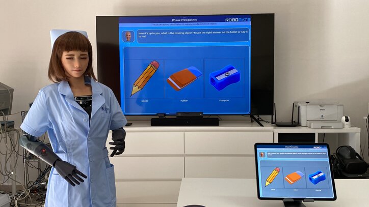 Humanoid robot in therapy setting with cognitive rehabilitation tools and RoboMate display.