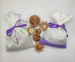 Sacchetti in tessuto bianco con decorazioni viola e biscotti in legno intagliati, prodotti naturali.