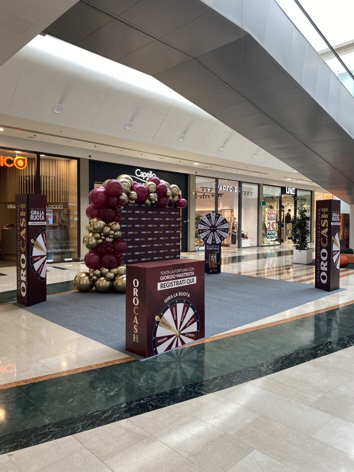 Allestimento in centro commerciale con stand promozionale Oro Cash e decorazioni a palloncini