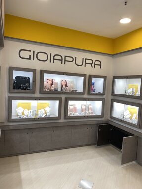 Esposizione di gioielli in uno showroom moderno con logo Gioiapura su parete gialla.