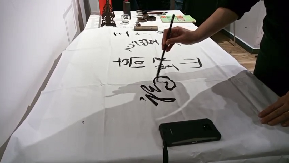 Person practicing Chinese calligraphy on a table, focusing on Mandarin learning.
