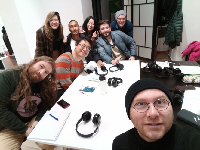 Group of people around a table with notebooks and headphones, smiling and posing for a picture.