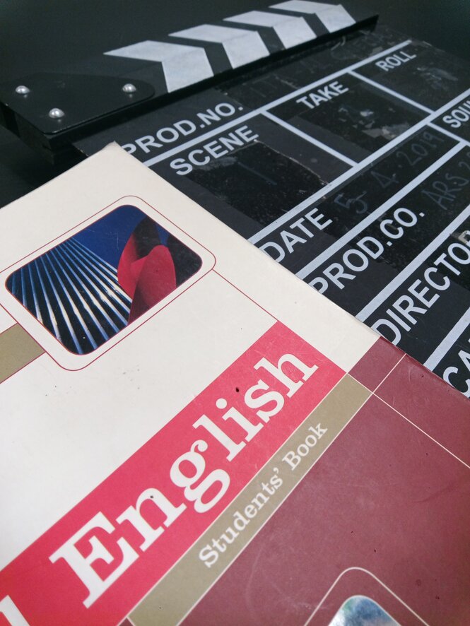 English textbook and film clapperboard, symbolizing language learning and creative storytelling. English textbook and film clapperboard, symbolizing language learning and creative storytelling.
