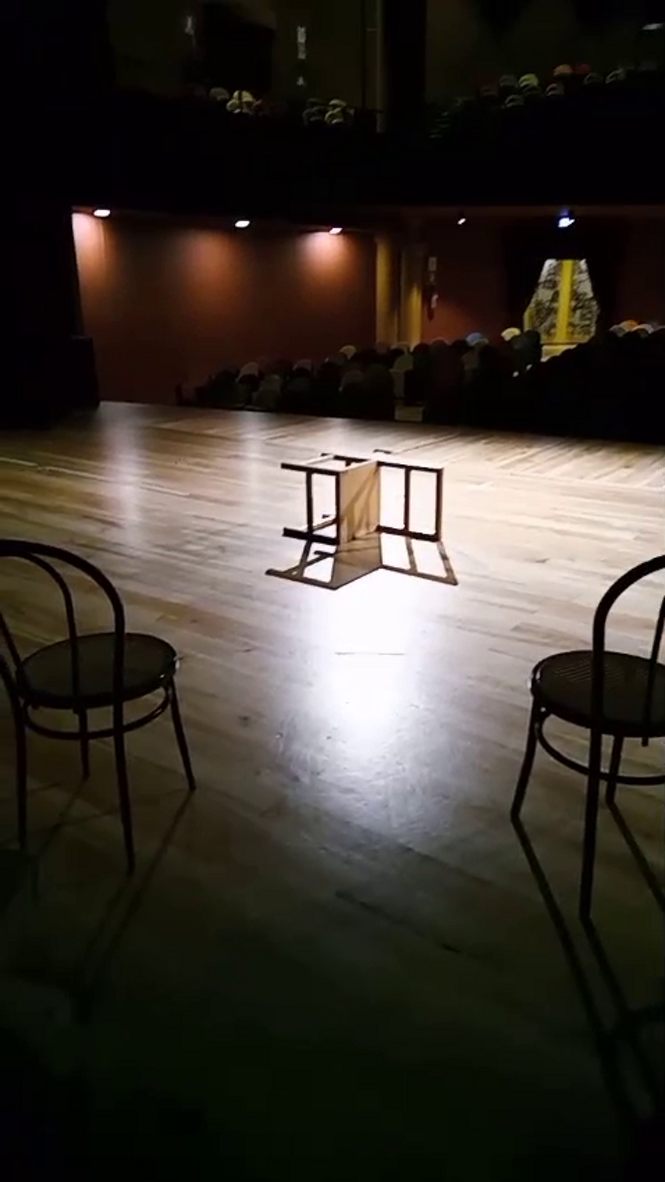 Dimly lit theater stage with chairs and a small table, Italian theater course setting