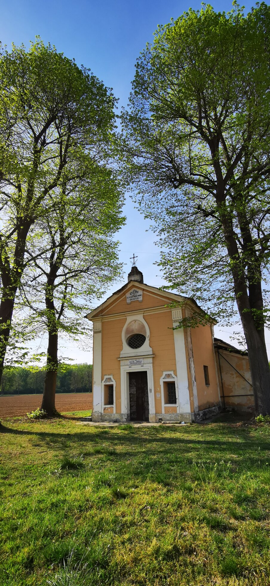 Cappella immersa nel verde con alberi alti, cielo azzurro sullo sfondo Cappella immersa nel verde con alberi alti, cielo azzurro sullo sfondo