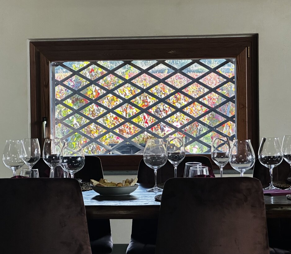 Indoor tasting setup with wine glasses at a vineyard with autumn leaves visible through the window.