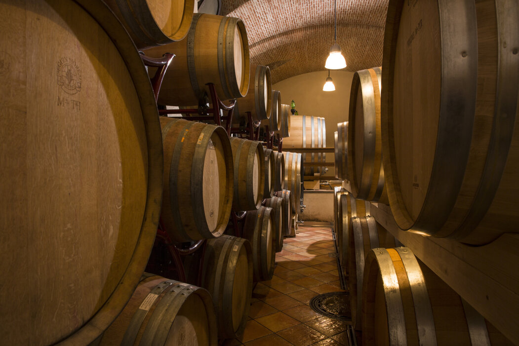 Wine barrels in a dimly lit cellar with brick ceiling.