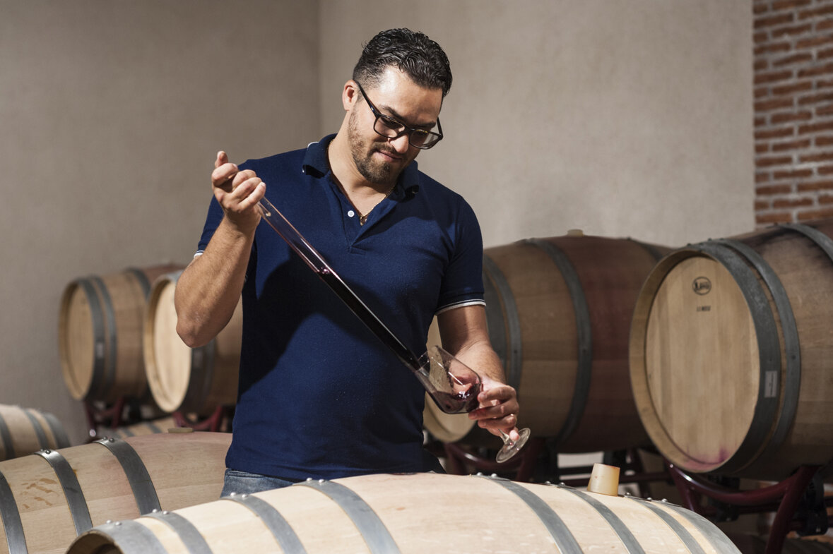 Winemaker tasting volcanic wine from barrel in cellar with Sicilian wine barrels in background.