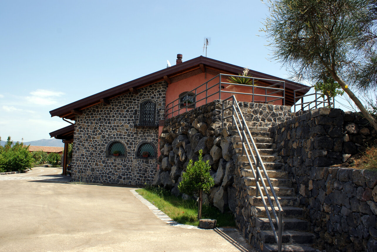 Rustic stone house with stairs and railing under a blue sky.