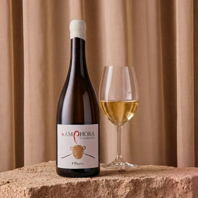 Bottle of white wine next to a glass on a stone surface.